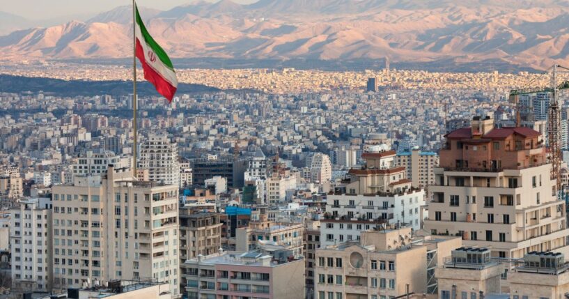 An Iran flag waving in front of the Tehran skyline.