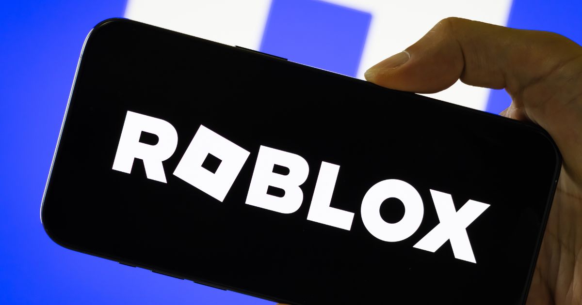 In this photo illustration, a person holds a smartphone displaying the logo of Roblox Corporation, a global online gaming and game creation platform, with the company's branding visible in the background, on July 29, 2025, in Chongqing, China.