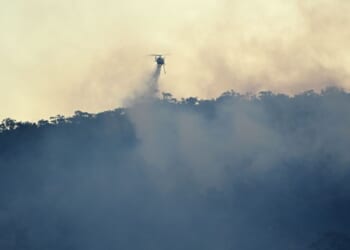 A helicopter drops water on a bushfire burning on the hills of Emu Heights in the Blue Mountains on Oct. 2, 2025.