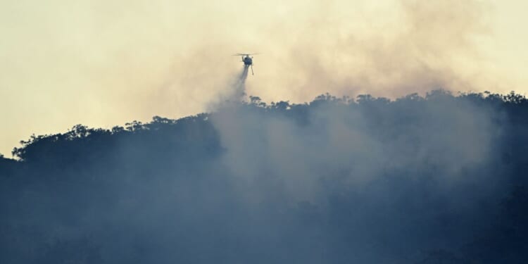 A helicopter drops water on a bushfire burning on the hills of Emu Heights in the Blue Mountains on Oct. 2, 2025.
