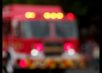 A Fire Engine heads down a street in a small town with its lights flashing.