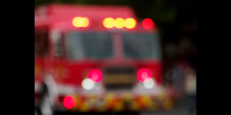 A Fire Engine heads down a street in a small town with its lights flashing.