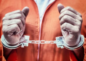 This stock image shows a handcuffed prisoner in an orange jumpsuit.