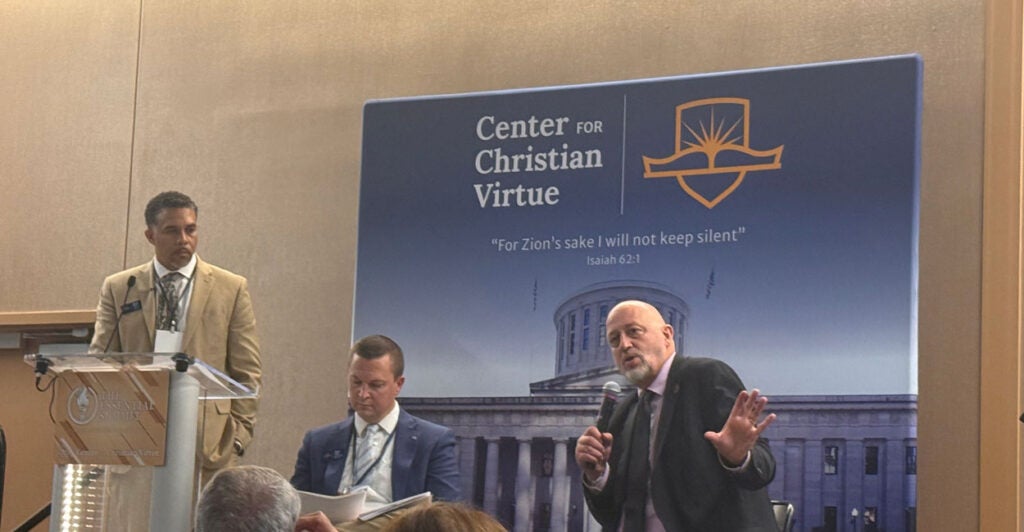State Rep. Gary Click sits in front of a banner for the Center for Christian Virtue at their Essential Summit. 