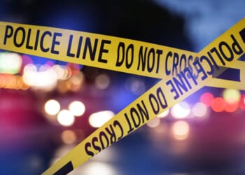 This Getty stock image shows police tape in the foreground of a crime scene at night.