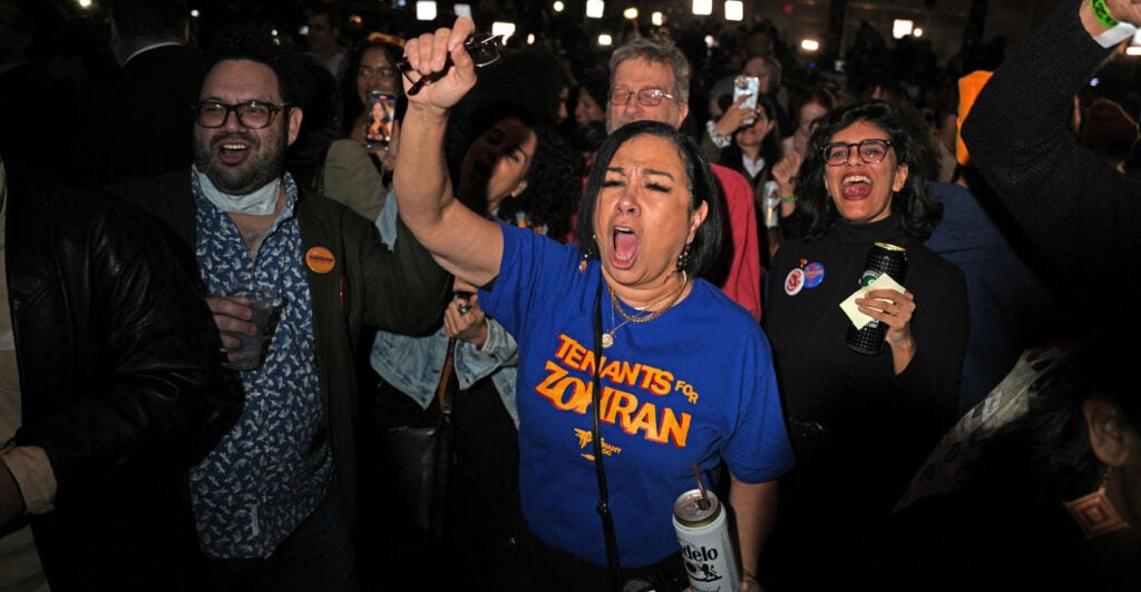 Zohran Mamdani supporters, wearing political t-shirts and holding alcoholic beverages, celebrate his victory at the Brooklyn Paramount Theater.