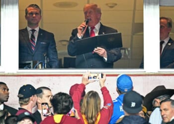 President Donald Trump, center, alongside Secretary of Defense Pete Hegseth, left, and Washington Commanders owner Josh Harris, right, reads the oath for people re-enlisting to the U.S. Army Sunday as he attends the NFL game between the Washington Commanders and the Detroit Lions in Landover, Maryland.