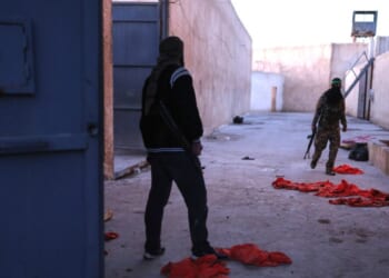 Syrian government fighters walk inside Al-Shaddadi prison, where red detainee suits lie on the ground, in the town of Shaddadeh, northeastern Syria, on Tuesday, a day after Syria's Interior Ministry said Islamic State group members escaped from the facility during clashes with the Kurdish-led Syrian Democratic Forces.