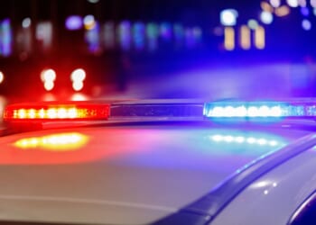 Police lights flash on top of a police car in a city at night.