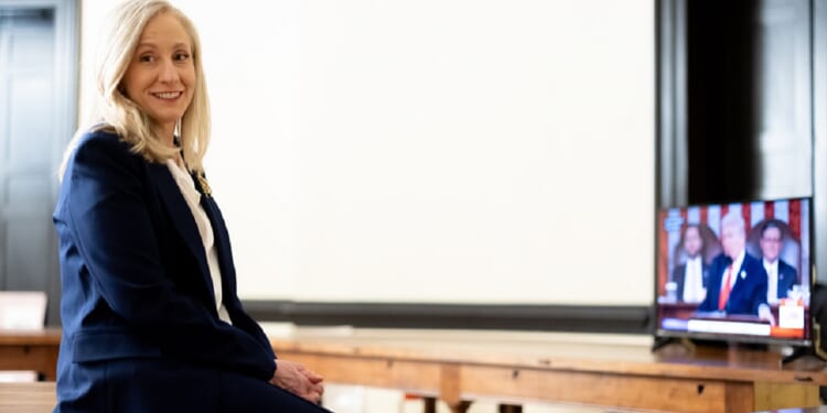 Virginia Gov. Abigail Spanberger leans against a table while President Donald Trump's delivers his State of the Union address on television.