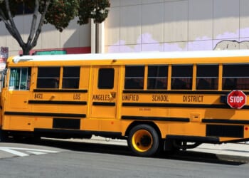 A Los Angeles Unified School District yellow school bus drives down the street in the daylight.