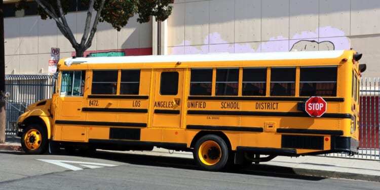A Los Angeles Unified School District yellow school bus drives down the street in the daylight.