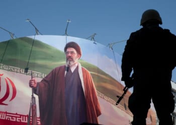 A member of the Iranian security forces stands guard under a large portrait of Iran's new Supreme Leader, Mojtaba Khamenei, during a memorial to mark the 40th day since his father, Ali Khamenei, was killed in U.S.-Israeli joint strikes on April 9, 2026, in Tehran, Iran.