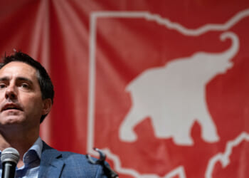Ohio Secretary of State Frank LaRose speaks in front of a red banner with an elephant inside a map of Ohio.