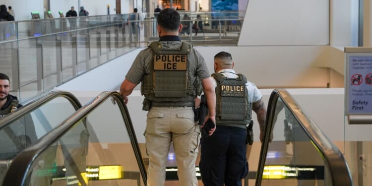 Two ICE agents ride down an escalator at LaGuardia Airport in New York on March 28, 2026.