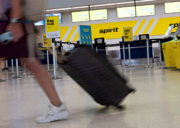 A woman drags her luggage past an empty Spirit Airlines counter at an airport.