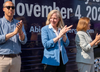 Abigail Spanberger, flanked by Jay Jones and Ghazala Hashmi clap in front of bus during campaign rally.