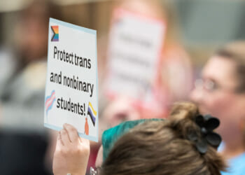 A person holds a sign reading, "Protect trans and nonbinary students!"