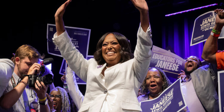 D.C. Democrat mayoral primary winner Janeese Lewis George in white pant suit waves both hands to supporters.