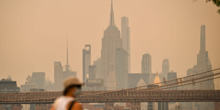 A person wearing a facemark walks near the Brooklyn Bridge as wildfire smoke from Canada causes hazy conditions on July 16, 2026 in New York. Out-of-control wildfires were raging Thursday in the Canadian province of Ontario, prompting evacuations and sending dangerous smoke billowing into the United States where millions of people were exposed to the unhealthy air.
