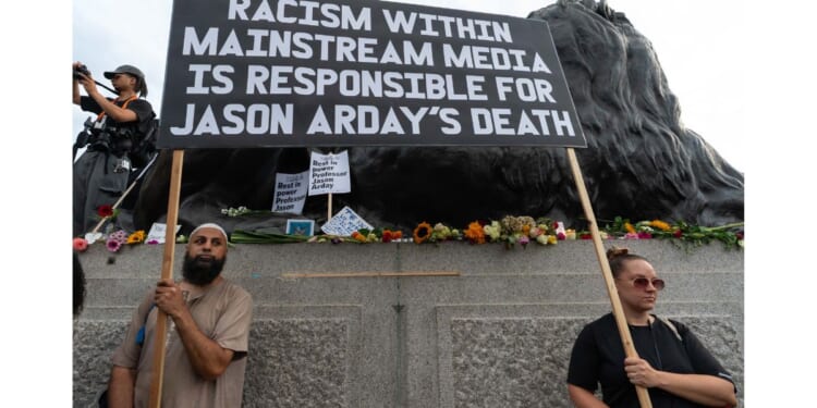 Two protesters hold a large placard blaiming the media for the death of Jason Arday Monday during a vigil in London's Trafalgar Square.