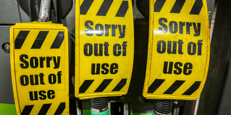 Three yellow signs with black stripes read Sorry out of use, covering the handles of fuel pumps at a gas station, indicating they are not available for service.