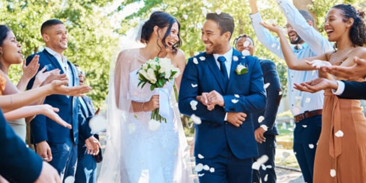 A couple gets married outdoors as attendees throw flower petals on them.