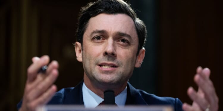 Senator Jon Ossoff appears in a suit and speaks into a microphone, gesturing with his hands during the Senate hearing questioning the Director of National Intelligence nominee Jay Clayton.