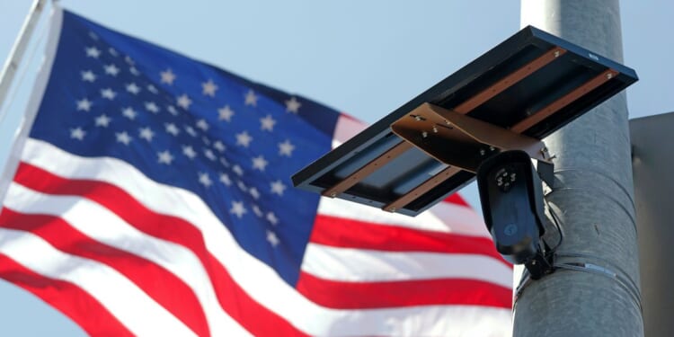 A Flock Safety camera is shown mounted in front of an American flag.
