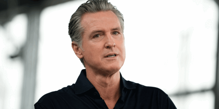 A man with gray hair, wearing a dark collared shirt, speaks while looking slightly off camera. The background is blurred, suggesting an indoor or semi-outdoor setting.