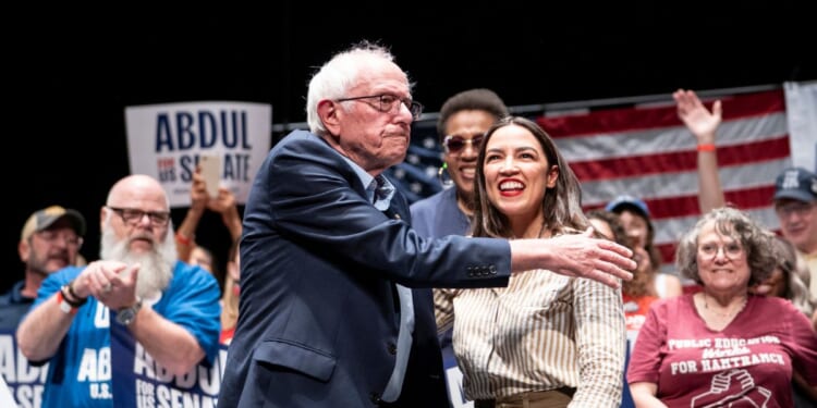 Sen. Bernie Sanders greets Rep. Alexandria Ocasio-Cortez at The People v. The Powerful rally at the Detroit Opera House on July 18, 2026, in Detroit, Michigan.