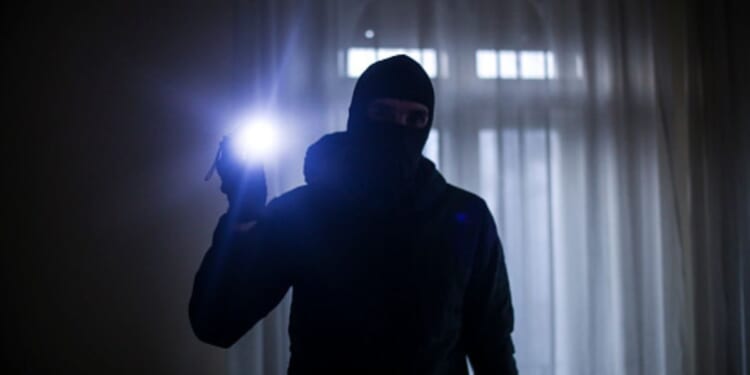 A burglar shines a bright flashlight in a dark house.