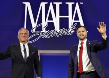 Two men in suits stand on stage, waving, in front of a blue backdrop with MAHA Summit written in large white letters.