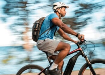 A man rides his electric bicycle on a trail near a body of water.