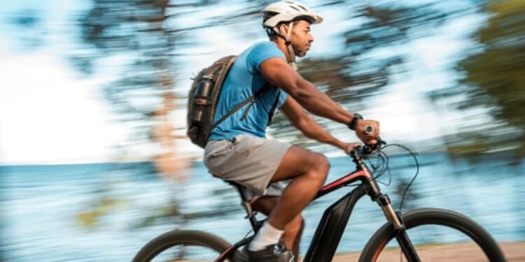 A man rides his electric bicycle on a trail near a body of water.