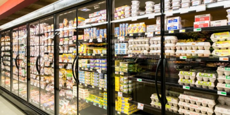 Fridges in a grocery store aisle are illuminated by light.