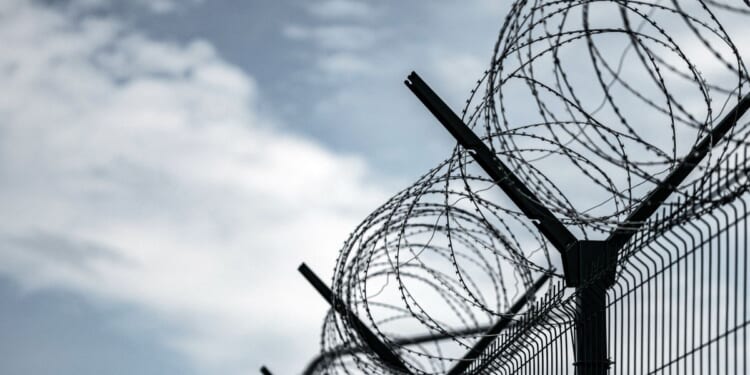 A prison fence with razor wire against a dark sky.
