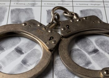 A pair of handcuffs sit on a paper of thumb prints.