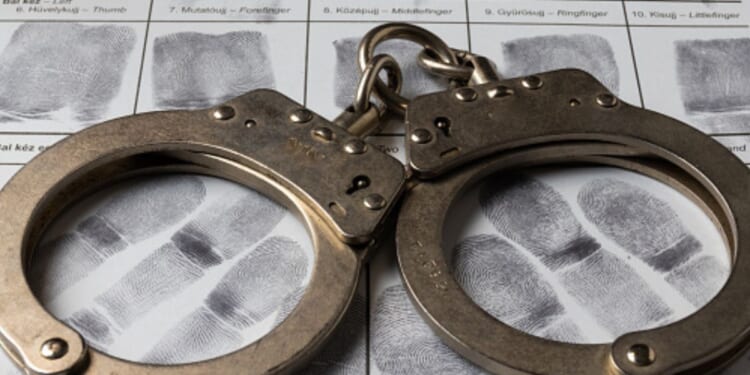 A pair of handcuffs sit on a paper of thumb prints.