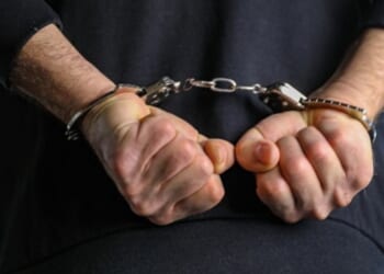 A man is pictured handcuffed in a dark blue shirt.