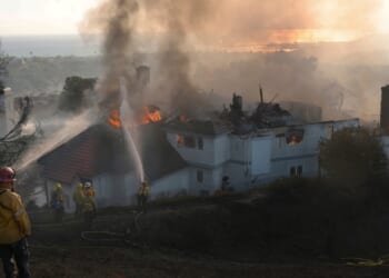 Firefighters spray water on a burning home engulfed by the Norte Fire moving through Southern California on Oct. 16, 2026.