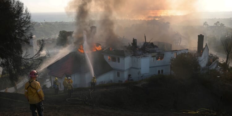 Firefighters spray water on a burning home engulfed by the Norte Fire moving through Southern California on Oct. 16, 2026.