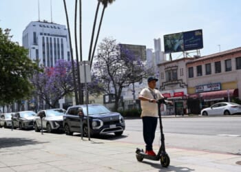 A pedestrian rides an electric scooter along Wilshire Boulevard in the Mid-Wilshire neighborhood on June 11, 2025, in Los Angeles, California.