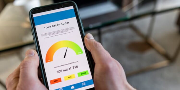 A phone with a credit score displayed on the screen is pictured in a man’s hand.