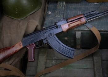 An AK-47 rifle lays on a military box above ammunition.