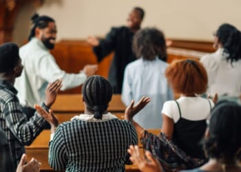 A group of churchgoers is singing and raising their hands while praying together.