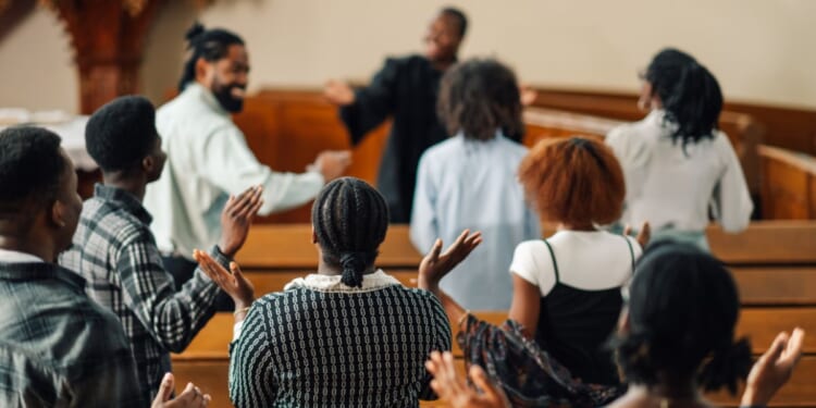 A group of churchgoers is singing and raising their hands while praying together.